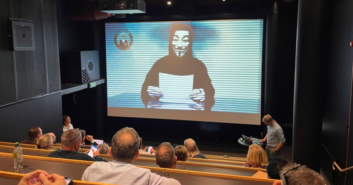 Event fra Hele Norge øver. I en forelæsningssal, på projektoren er en hacker med Guy Fawkes maske på